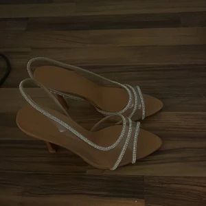 Beige klackskor med strassdetaljer - Eleganta beige klackskor med transparenta remmar dekorerade med glittrande strass. 