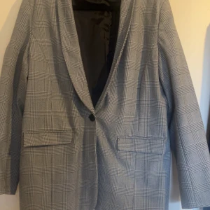 Grå rutig kavaj från KappAhl - Snygg grå rutig kavaj från KappAhl i storlek L. Kavajen har en klassisk design med en knapp framtill och två fickor. Perfekt för en stilren look. Använd fåtal gången och tar mest plats i garderoben.