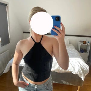 Svart ribbad halterneck topp - Säljer en snygg svart ribbad halterneck topp. Toppen är ärmlös och har en tight passform som framhäver figuren. Perfekt för varma sommardagar eller en kväll ute. Den är enkel att matcha med både jeans och kjol.