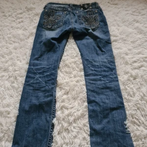 Blå jeans med broderad detalj från Miss Me - Snygga blå jeans från Miss Me med en unik broderad detalj på bakfickorna. De är bootcut! Jeansen har också dekorativa nitar som ger extra stil. Super fina och passar till alla möjliga tillfällen! Midjemått: 42 cm Innerbenslängd: 79 cm. Tveka inte att skriva!💗