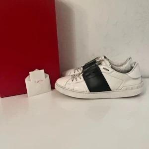 Valentino open - Snygga Valentino sneakers i vitt med en bred svart rem över snörningen. Skorna har en stilren design med klassiska detaljer och en bekväm passform. Perfekta för en trendig look. Storlek 42 passar 43. Alla og saker på bilderna följer med!