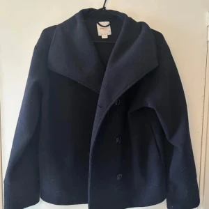 Svart kappa - Snygg svart kappa med knappar och bred krage. Perfekt för kyligare dagar och ger en stilren look. PRIS KAN DISKUTERAS!!!