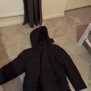 Svart pufferjacka från Studio Total - Säljer en svart pufferjacka från Studio Total i storlek L. Jackan har en huva och dragkedja framtill. Perfekt för kyliga dagar med sin vadderade design. Huvan går att ta av helt. 