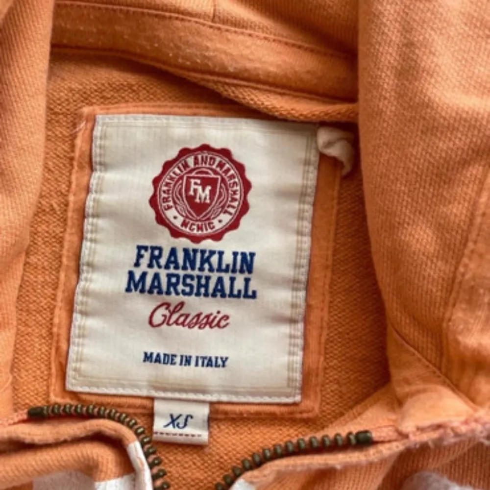 Säljer en snygg orange hoodie från Franklin Marshall med dragkedja och vit logga på bröstet. Den har en justerbar huva med vita snören och ribbade muddar vid ärmslut och nederkant. Perfekt för en avslappnad stil! Storlek XS. Neuletakit & Villapaidat.