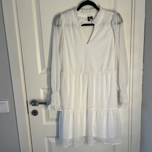 Vit klänning från Vero Moda - Säljer en söt vit klänning från Vero Moda med långärmad design och v-ringning. Klänningen har ett diskret prickigt mönster och volangdetaljer vid ärmslut och nederkant. Perfekt för en somrig look! 💫