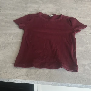 Vinröd ribbad topp - Vinröd ribbad topp från Cubus med korta ärmar och rund hals. T-shirten har en croppad passform och lätt vågig kant nertill. Perfekt för dig som gillar en enkel men snygg stil.