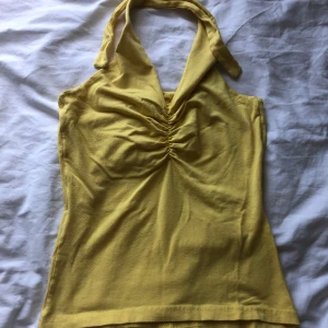 Gul halterneck topp från Bik Bok - Snygg gul halterneck topp från Bik Bok i mjuk bomull. Toppen har en djup v-ringning med rynkade detaljer framtill och knyt runt nacken. Perfekt för varma dagar och ger en fräsch vibe till din outfit.