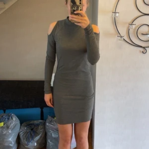 Grå klänning Gina Tricot - Grå ribbad kortklänning från Gina Tricot med lång ärm och trendiga cut out-detaljer på axlarna. Tight passform och hög hals, perfekt för dig som gillar en stilren look med en twist. Väldigt mjuk och bekväm🩶