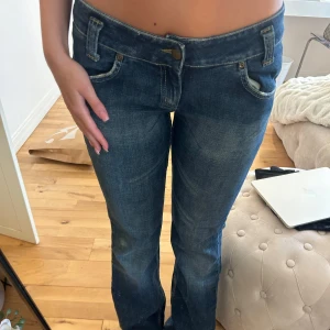 Blå low Waist bootcut jeans från Lee - Snygga blå jeans från Lee med bootcut passform och låg midja. Jeansen har klassiska fem fickor, slitna detaljer och Lee-logga bak på linningen. Perfekta för dig som gillar en avslappnad och tidlös stil.