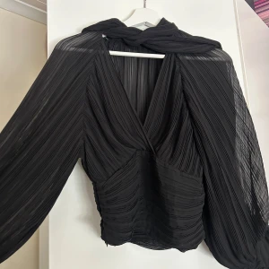Svart blus med knyte  - Skitsnygg svart blus från Zara med v-ringning och långa, transparenta ärmar i storlek XS. Blusen har knyte vid halsen som en scarf och går ihop vid handledarna med knappar. Ena knapphållaren har en liten defekt som fanns när jag köpte den, därav priset. Använd fåtal gånger iprincip nyskick i materialet. 