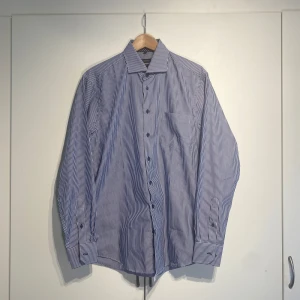 Erla Of Sweden Blåvit randig skjorta  - Klassisk blå och vit randig skjorta från Erla of Sweden. Skjortan har en snygg krage och är tillverkad i bomull, perfekt för en clean och stilren look. Storlek L. Skriv för fler bilder 