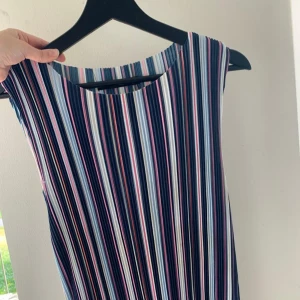 Randig långklänning i färgglada toner - Säljer en ärmlös långklänning med vertikala ränder i blått, vitt, rosa och lila. Klänningen har rund halsringning och ett flowy fall, perfekt för dig som gillar färg och mönster. Superenkel att styla med sneakers eller sandaler.