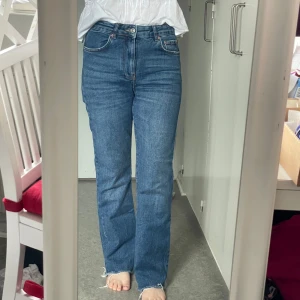 Blå raka jeans med rå kant - Säljer ett par klassiska blå jeans med raka ben och hög midja. Jeansen har rå, fransig kant nertill för en avslappnad vibe. Perfekta till sneakers eller boots och passar till allt.