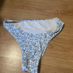Blåblommiga bikinitrosor - Snygga bikinitrosor med blått blommönster på vit botten. Modellen har hög skärning och klassisk passform, perfekt för strandhäng. Tunt och smidigt material som torkar snabbt.