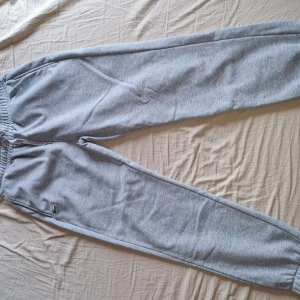 Grå mjukisbyxor med broderad detalj - Snygga grå mjukisbyxor med elastisk midja och en liten broderad grön detalj vid benet. Byxorna har en avslappnad passform och är perfekta för chill dagar. Mjukt material som känns skönt mot huden.