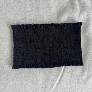 Svart bandeau tubtopp - En svart bandeau tubtopp med smockad struktur och volangkant upptill och nedtill. 