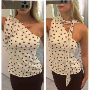 Prickig one shoulder topp med scarfdetalj - Vit one shoulder topp med svarta prickar och en lång scarfdetalj som kan knytas på olika sätt. Aldrig använd! Slutsåld på H&M