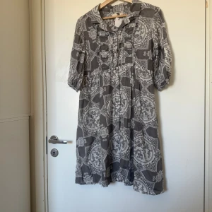 Gråvit mönstrad kortklänning - Kortklänning i grått och vitt med unikt mönster och volangdetaljer framtill. Klänningen har krage, knappar och halvlånga ärmar med resår. Luftigt material, perfekt för en chill och trendig look. Från märket Odd Molly i storlek 2 som enligt deras storleksguide motsvarar en storlek M. Mycket fint skick, jag hittar inga synlig anmärkningar eller defekter. 