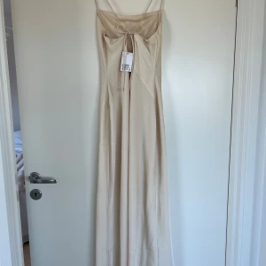 Satin klänning hm - Supersnygg långklänning i champagnefärg från Hm. Klänningen har tunna axelband, smickrande passform och en fin knytning framtill. Perfekt för dig som gillar minimalistisk och elegant stil. Materialet känns mjukt och följsamt mot kroppen.