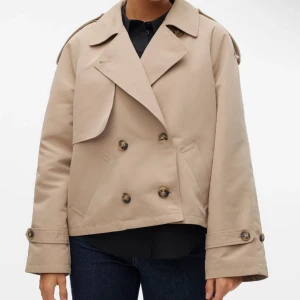 Beige kort trenchcoat med knappar!!! - Snygg kort trenchcoat i beige med dubbelknäppning och bred krage. Helt Ny! Storlek M, prislappen är kvar, aldrig använd (bara provat)💓 