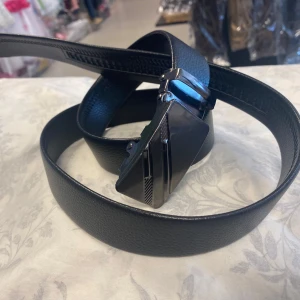 Svart skärp med metallspänne - Stilrent svart bälte i skinn med bred, rektangulär metallspänne i borstat silver. Spännet har olika geometriska mönster och detaljer som ger en modern och edgy känsla. Perfekt accessoar för att lyfta din outfit med en clean look. 169kr/st 