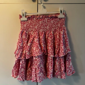 Rosa blommig volangkjol Samsa XS - Supersöt kort volangkjol från Samsa Collection i rosa och vitt med blommigt mönster. Kjolen har smock i midjan och flera lager volanger som ger en riktigt flowy och lekfull vibe. Perfekt för dig som gillar färg och mönster! Kjolen säljs eftersom den är för kort för mig nu. Katt finns i hemmet, tvättas innan den skickas ut! Kontakta för fler frågor!🌷 