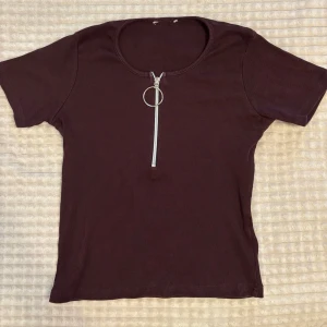 Mörkbrun ribbad topp med dragkedja - Snygg mörkbrun ribbad topp med korta ärmar och rund halsringning. Inga skador. Storlek xs
