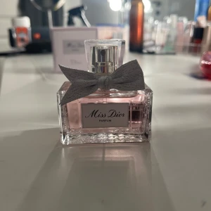 Miss Dior Parfum 35 ml med ask - Miss Dior Parfum i elegant glasflaska med ljusrosa doft och en söt grå rosett runt halsen. Flaskan rymmer 35 ml och kommer med originalask i matchande ljusrosa färg. Perfekt för dig som gillar lyxiga och feminina parfymer. Andvänd en gång