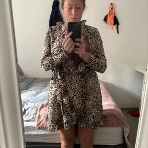 Leopardmönstrad omlottklänning Ally Bell - Så Snygg kort omlottklänning om jag hade varit lite mindre hade jag aldrig sålt den, jag är storlek M så den passar S. men försökt visa den ändå på! Så fin vid brösten, nere vid volangen vid ovan knä  från Ally Bell med leopardmönster i beige, svart och brunt. Klänningen har långa ärmar, volangkant och knyt i midjan. Perfekt för dig som vill sticka ut med en trendig look.