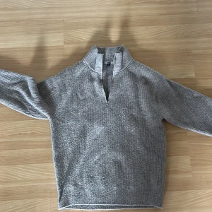 Grå ribbstickad half zip-tröja Uniqlo - Mysig grå/beige ribbstickad tröja från Uniqlo i storlek S. Tröjan har en hög krage med half zip-dragkedja och långa ärmar. Materialmix med akryl, polyamid, ull och elastan ger en skön känsla. Perfekt för lager-på-lager under kyliga dagar.