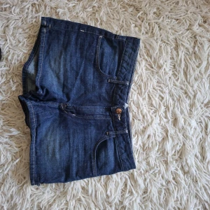 Mörkblå jeansshorts med fickor - Snygga mörkblå jeansshorts med klassisk femficksdesign och knappstängning framtill. Shortsen har en rak passform och är perfekta för varma dagar. Tidlös denimlook som funkar till allt och ger en avslappnad vibe.