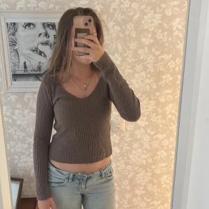 Brun ribbad stickad tröja v-ringad - Mysig brun stickad tröja med ribbad struktur och v-ringad hals. Modellen är croppad och har långa ärmar, perfekt för lager-på-lager under höst och vinter. Enkel att matcha med jeans eller kjol för en chill look.