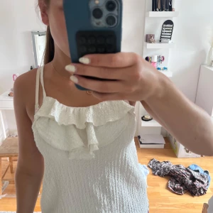 Vit volangtop från Zara - Supersöt vit linnetopp från Zara med smockad struktur och volangdetalj framtill. Tunt och lätt material, perfekta smala axelband och en luftig känsla. Passar perfekt till jeans eller kjol för en fräsch sommarlook.