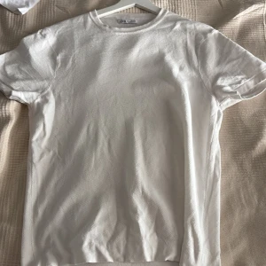 Vit t-shirt från Zara i bomull - Klassisk vit t-shirt från Zara i storlek M. T-shirten har rund halsringning, korta ärmar och är tillverkad i ett mjukt bomullstyg med diskret struktur. Perfekt basic-plagg att ha i garderoben.