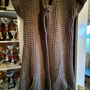 Stickad brun klänning kofta  från b.young - Mysig stickad klänning i brun nyans från b.young. Modellen är ärmlös med grovstickad struktur och har en hög krage. Perfekt för lager-på-lager och chill höst- eller vinterstil.