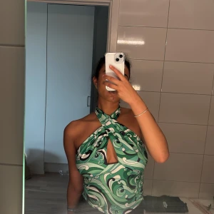 Grön swirl halterneck topp - Säljer en snygg halterneck topp med grönt, svart och vitt swirlmönster. Toppen har omlott-detalj framtill och en öppen rygg. Perfekt för dig som gillar statement-plagg med cool retrovibe.