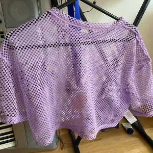 Ljuslila meshtröja med kort ärm rave festival 90s - Säljer en ljuslila meshtröja med oversized passform. Tröjan är stickad i ett grovmaskigt nätmönster och har korta ärmar. Perfekt att slänga över ett linne eller bikini för en chill och trendig look.