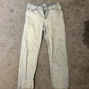 Ljusblå jeans från Grunt - Säljer ett par ljusblå jeans från Grunt med klassisk femficksdesign och raka ben. Jeansen har orangea sömmar, bälteshällor och stängs med knapp och dragkedja. Perfekta för en avslappnad och stilren look.