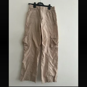 Beiga cargopants med fickor - Säljer ett par beiga cargopants med bred passform och stora fickor på sidorna. Byxorna har resår i midjan och vid benslut, samt flera praktiska fickor både fram och bak. Perfekta för en avslappnad och trendig look.