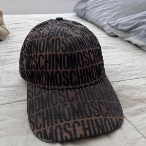 Moschino keps - Snygg brun keps från Moschino. Justerbar baktill med Moschino-detalj. Säljer då den inte kommer till användning något mer.