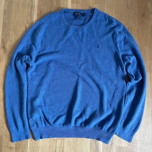 Blå bomullströja från Polo Ralph Lauren - Snygg blå tröja från Polo Ralph Lauren i mjuk pima bomull. Klassisk rund halsringning, diskret broderad logga på bröstet och ribbade muddar vid ärmslut och nederkant. Perfekt för dig som gillar stilren och enkel design.