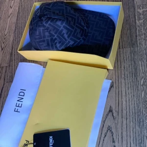 Svart Fendi keps med FF-mönster - Snygg svart keps från Fendi med ikoniskt FF-monogram i mörkgrått över hela kepsen. Justerbar rem baktill i skinn med Fendi-logga. Klassisk böjd skärm och exklusiv känsla, perfekt för dig som vill sticka ut med designeraccessoar.