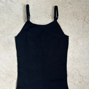 Svart shaper linnetopp med smala axelband - Enkel och stilren svart shaper linnetopp med smala justerbara axelband. Det är en shaper så den formar och tar in magen, ser väldigt bra ut när man väl sätter på sig önskad klänning/top. Kan även användas som en topp i sig.