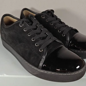 Svarta Lanvins - Stilrena svarta lanvins med ovandel i mocka och glansig lackad tå. Skorna har snörning och en platt sula, perfekt för en clean och modern look. Snygga detaljer med kombinationen av material som ger extra edge.