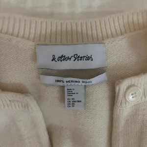 Beige merinoullskofta från & Other Stories - Supermjuk och stilren beige/vit kofta från & Other Stories. Nästan alltid slutsåld. Köpt för 790kr och säljer för 500kr. Kan tänka mig sänka priset!!