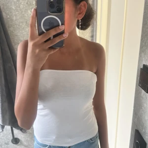 Vit bandeau tubtopp - Enkel och stilren vit bandeau tubtopp i mjukt material. Perfekt att matcha med jeans eller kjol för en clean look. Toppen är ärmlös och axelbandslös, vilket ger en snygg och minimalistisk vibe.