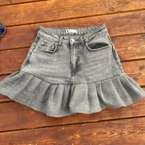 Grå jeanskjol med volang från Gina Tricot - Supersnygg grå jeanskjol från Gina Tricot med volangkant nertill. Kjolen har klassisk femficksdesign, dragkedja och knapp framtill samt en cool tvättad look. Perfekt för dig som gillar en trendig och avslappnad stil. Jag har sytt kjolen själv, men allt är noggrant gjort, har flera till kjolar till salu💖