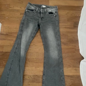 Grå bootcut jeans från Gina Tricot - Snygga grå jeans från Gina Tricot i bootcut-modell. Jeansen har slitna detaljer, klassisk femficksdesign och coola bakfickor med flik och knapp. Perfekta för dig som gillar en avslappnad men trendig look.