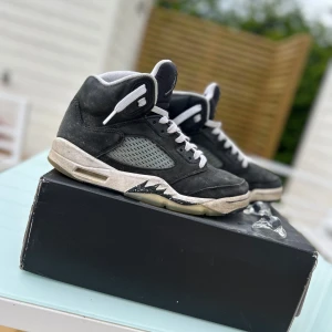 Nike Air Jordan 5 Retro Oreo - Säljer ett par feta Jordan 5 Oreo. Klassisk high-top siluett, lite sliten mocka på sidorna och vit snörning. Snygg kontrast mellan svart mocka och grå insida, samt ikoniska hajtandsdetaljer på sulan.                                      Perfekta för dig som gillar streetstyle🛹👟. Skorna köptes från footlocker och det ingår box samt Jordan 5:ornas klassiska snörning låsare.