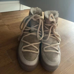 Beige moon boots från Inuikii - Säljer ett par snygga beige moon boots från Inuikii med grova snören och mjuk pälsfodring. Skorna har en rund tå, platt sula och är tillverkade i mocka och skinn. Perfekta för kalla dagar när du vill hålla stilen och värmen. Tog bilden från min vinted